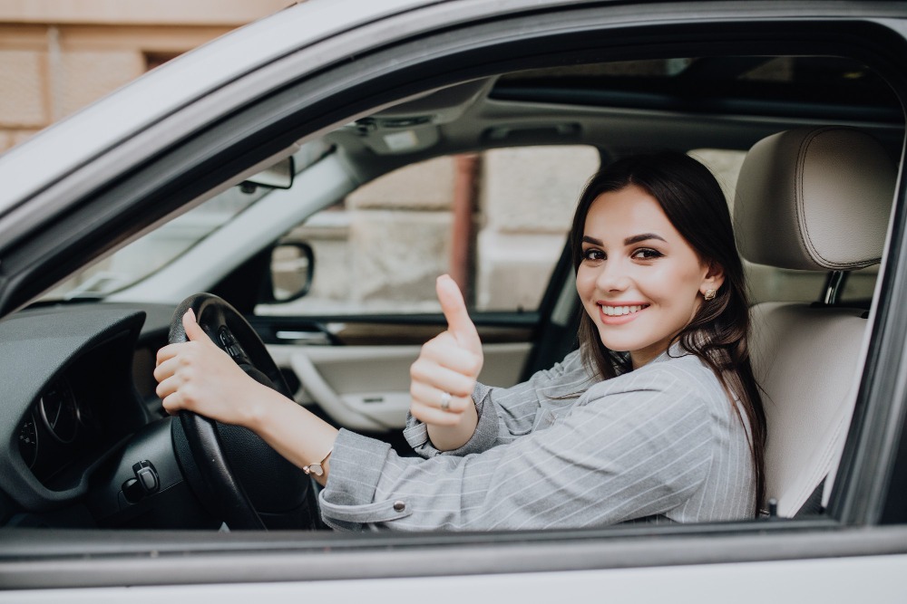 a woman sitting inside the car driving the steer wheel showing thumbsup sign