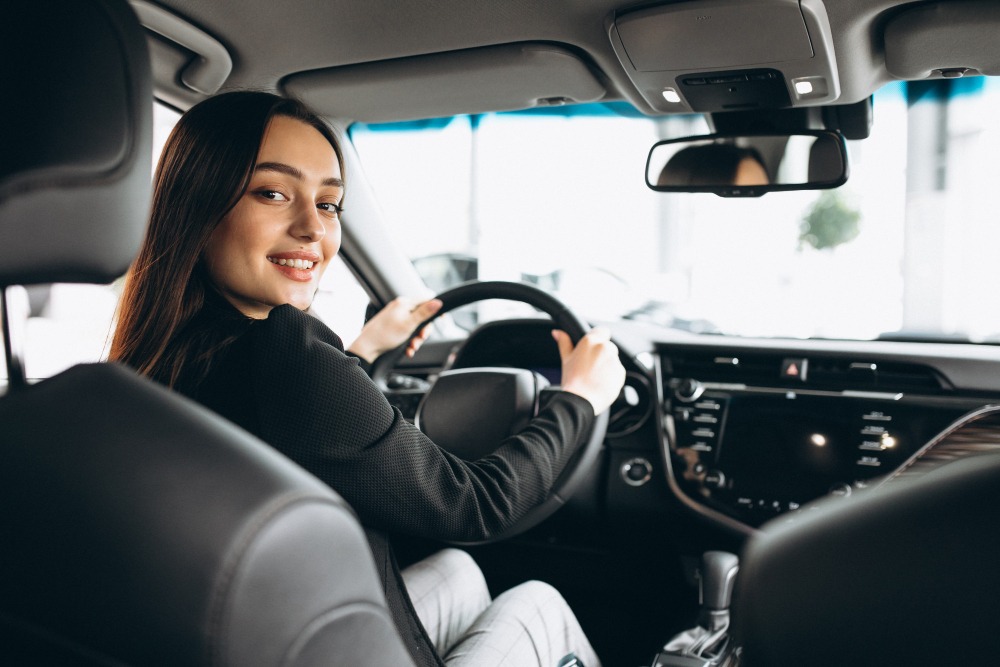 a lady sitting inside the car driving the steer wheel